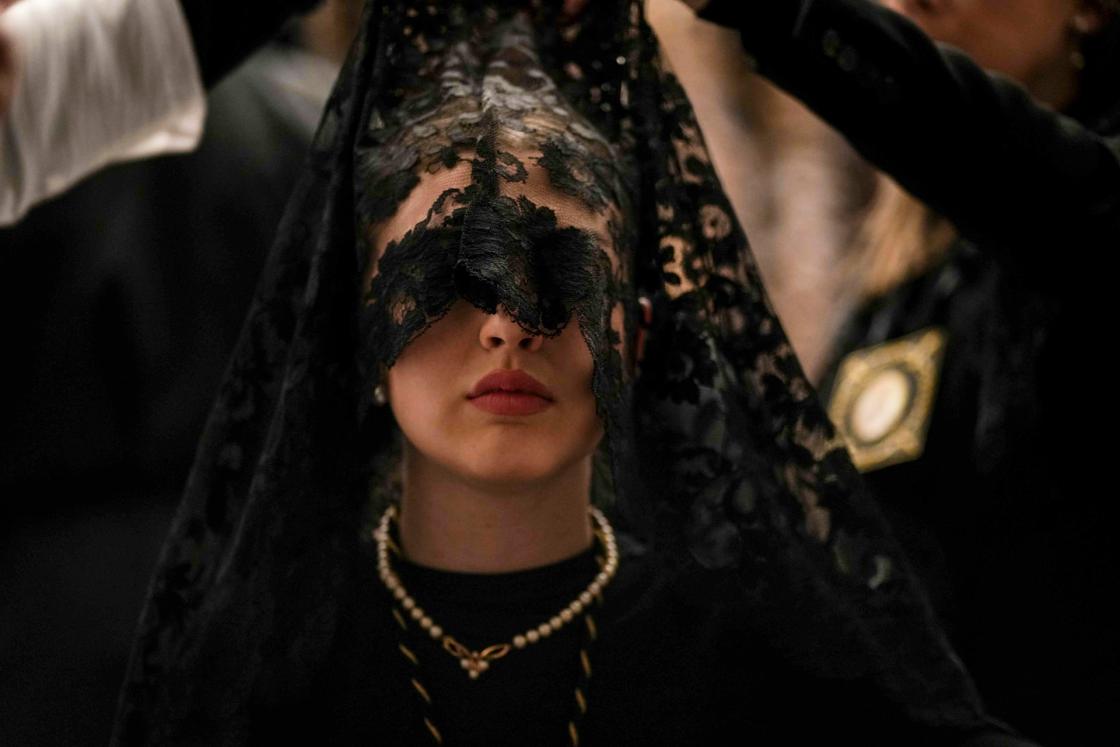 CÓRDOBA, 29/03/2024.- Una señora con mantilla de la Hermandad de Los Dolores, conocida como "La Señora de Córdoba", en la Iglesia de Capuchinos donde han comunicado finalmente la suspensión por lluvia de la procesión del Viernes Santo de 2024 en Córdoba, y una de las imágenes que forman parte de la exposición fotográfica comisariada por la Agencia EFE para los 'Spanish Days' en Arabia Saudí. EFE/Rafa Alcaide