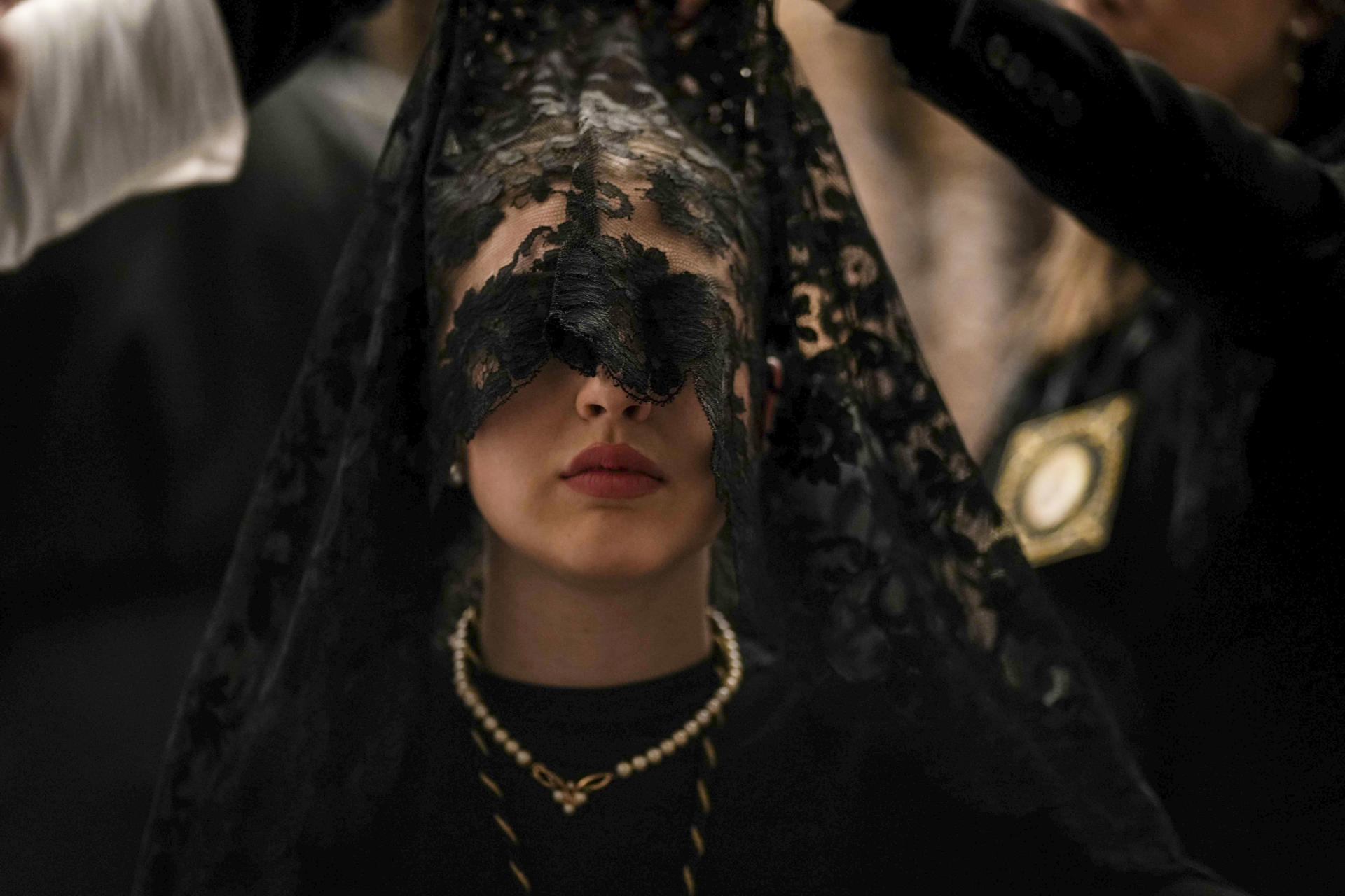 CÓRDOBA, 29/03/2024.- Una señora con mantilla de la Hermandad de Los Dolores, conocida como "La Señora de Córdoba", en la Iglesia de Capuchinos donde han comunicado finalmente la suspensión por lluvia de la procesión del Viernes Santo de 2024 en Córdoba, y una de las imágenes que forman parte de la exposición fotográfica comisariada por la Agencia EFE para los 'Spanish Days' en Arabia Saudí. EFE/Rafa Alcaide