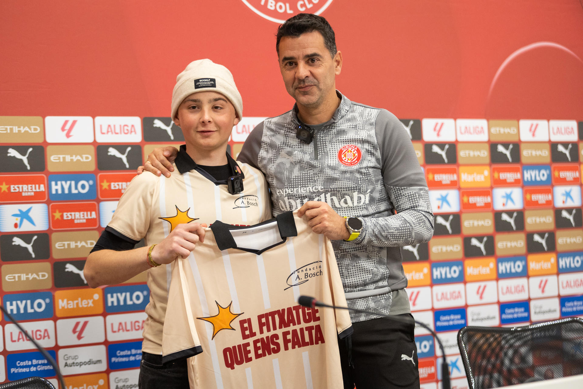 ¿Cuál cree que es el fichaje que nos falta?, es la pregunta que el pequeño Biel Pérez Soriano (i) le ha hecho este domingo al entrenador del Girona FC, Míchel (d), durante la rueda de prensa previa a la jornada de LaLiga y que ha formado parte de campaña de la Fundació Albert Bosch en el Día Mundial contra el Cáncer Infantil. EFE/IMAGEN CEDIDA/FUNDACIÓ ALBERT BOSCH/CRÉDITO OBLIGATORIO